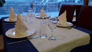 Een eettafel gedekt met borden, glazen en bestek, met uitzicht op een besneeuwd berglandschap.