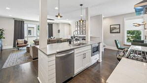 A modern kitchen with white cabinetry, a central island, and a dining area with a green chair. - Rooftop Terrace · Fire Pit · Wet Bar · City Views (Nashville)