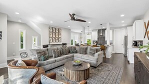 A modern living room with a sectional sofa, a round coffee table, and a ceiling fan. - Rooftop Terrace · Fire Pit · Wet Bar · City Views (Nashville)