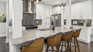 A modern kitchen with white cabinets, a large island with bar stools, stainless steel appliances, and pendant lighting. - Rooftop Terrace · Fire Pit · Wet Bar · City Views (Nashville)