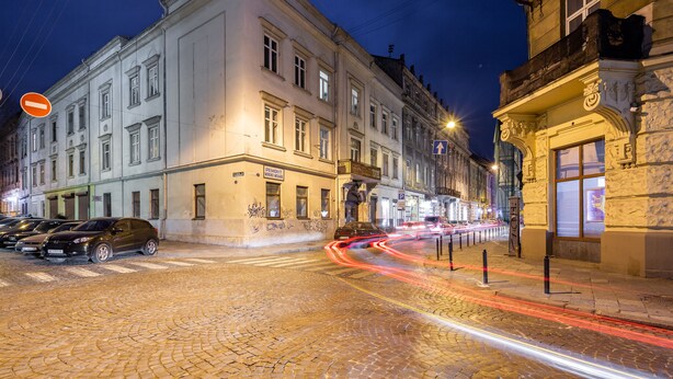 A cobblestone street at night with historic buildings, a no entry sign, and light trails from moving vehicles. - Apartments with bedrooms at the center (Lviv)