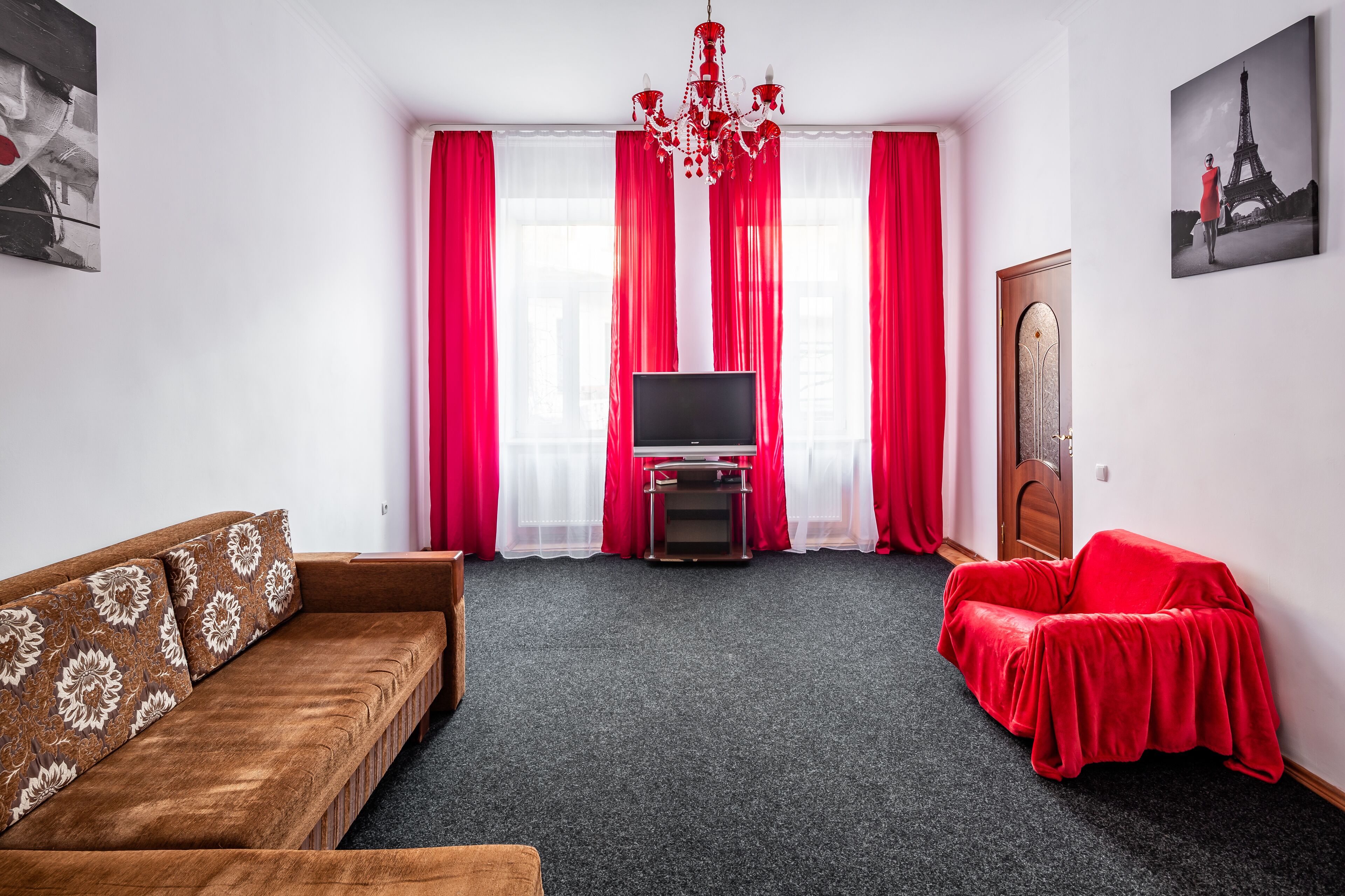 A living room with a brown sofa, a red armchair, a TV, and a red-covered table.
