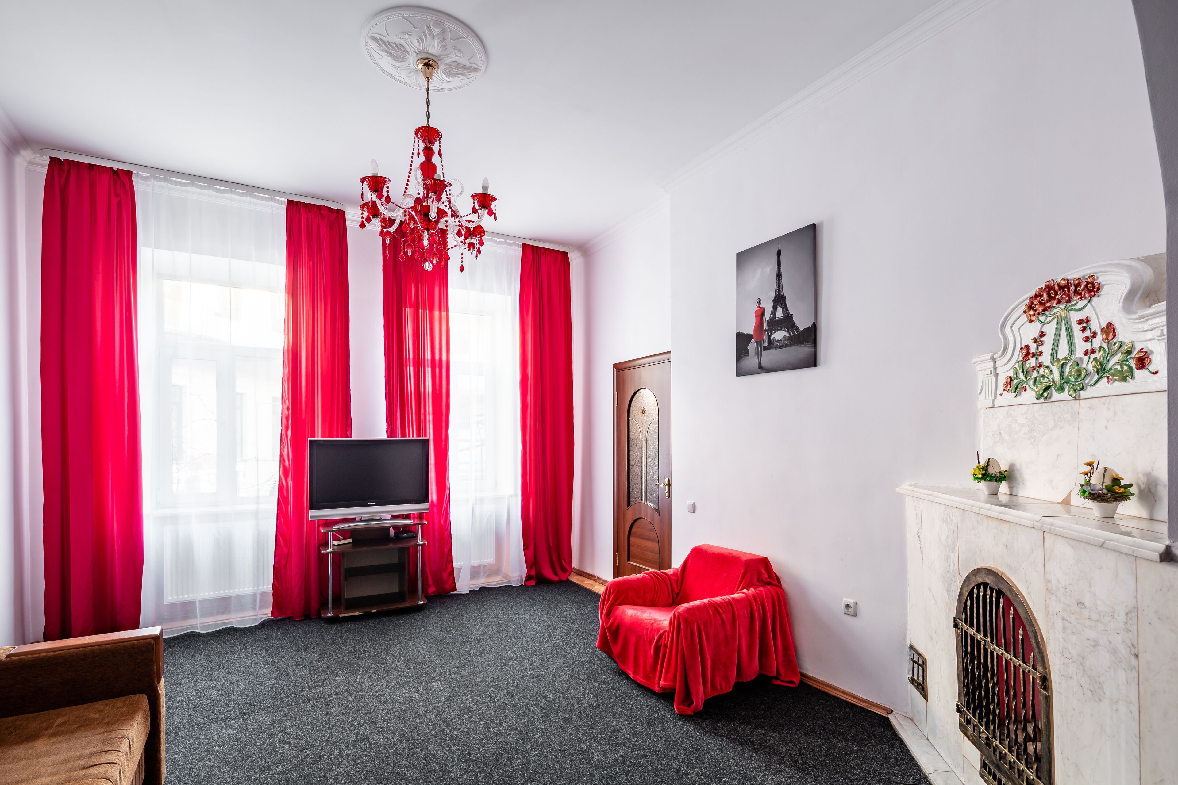 A room with a television, red curtains, a chandelier, a fireplace, and a door.
