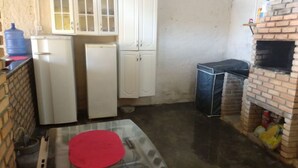 A kitchen with white cabinets, a refrigerator, a water dispenser, a brick oven, and a red mat on the floor. - Casa na praia do Romance Caraguatatuba (Caraguatatuba)