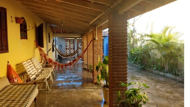 A covered outdoor area with a hammock, lounge chairs, and a brick wall. - Casa na praia do Romance Caraguatatuba (Caraguatatuba)
