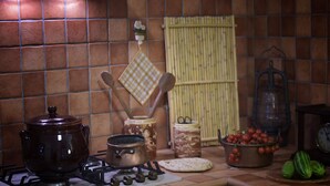 Una cocina con estufa, ollas, una cuchara de madera, un tazón de cerezas y un melón verde sobre la encimera.