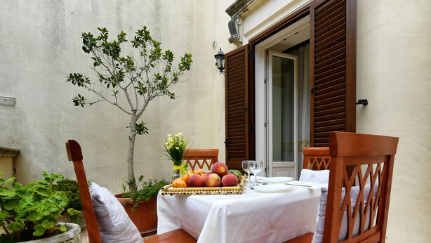 Una mesa servida con una cesta de fruta, una copa de vino y una pequeña planta en maceta.