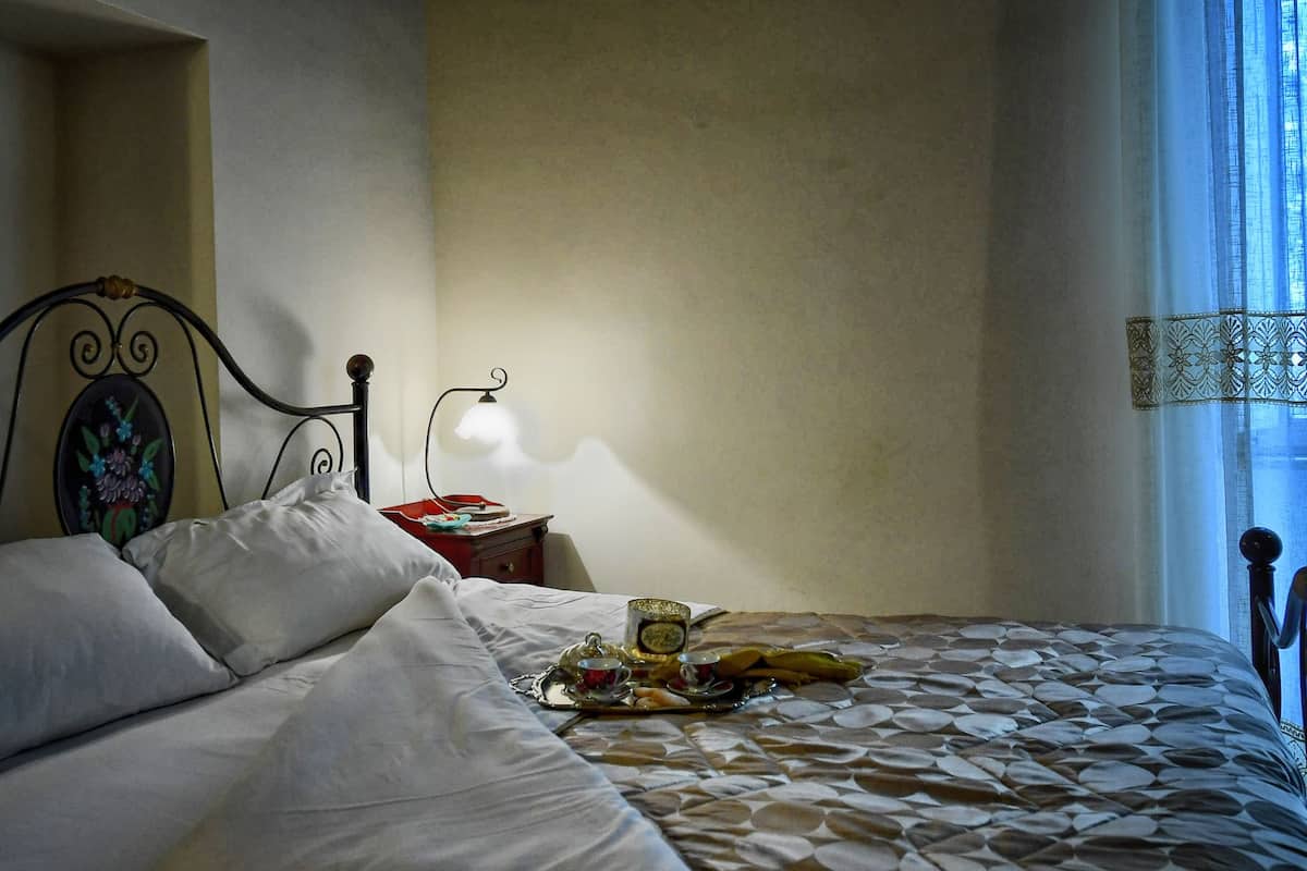 Ein ordentlich bezogenes Bett mit einem gemusterten Überwurf, ein Nachttisch mit Lampe und ein dekoratives Kopfteil.