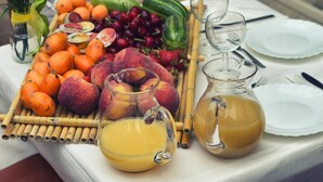 Una mesa con frutas, un jarro de jugo de naranja y un abacón con té.