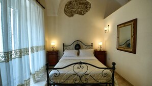 Un dormitorio con cama, dos mesitas de noche, un espejo adosado a la pared y un elemento decorativo de piedra sobre la cama.