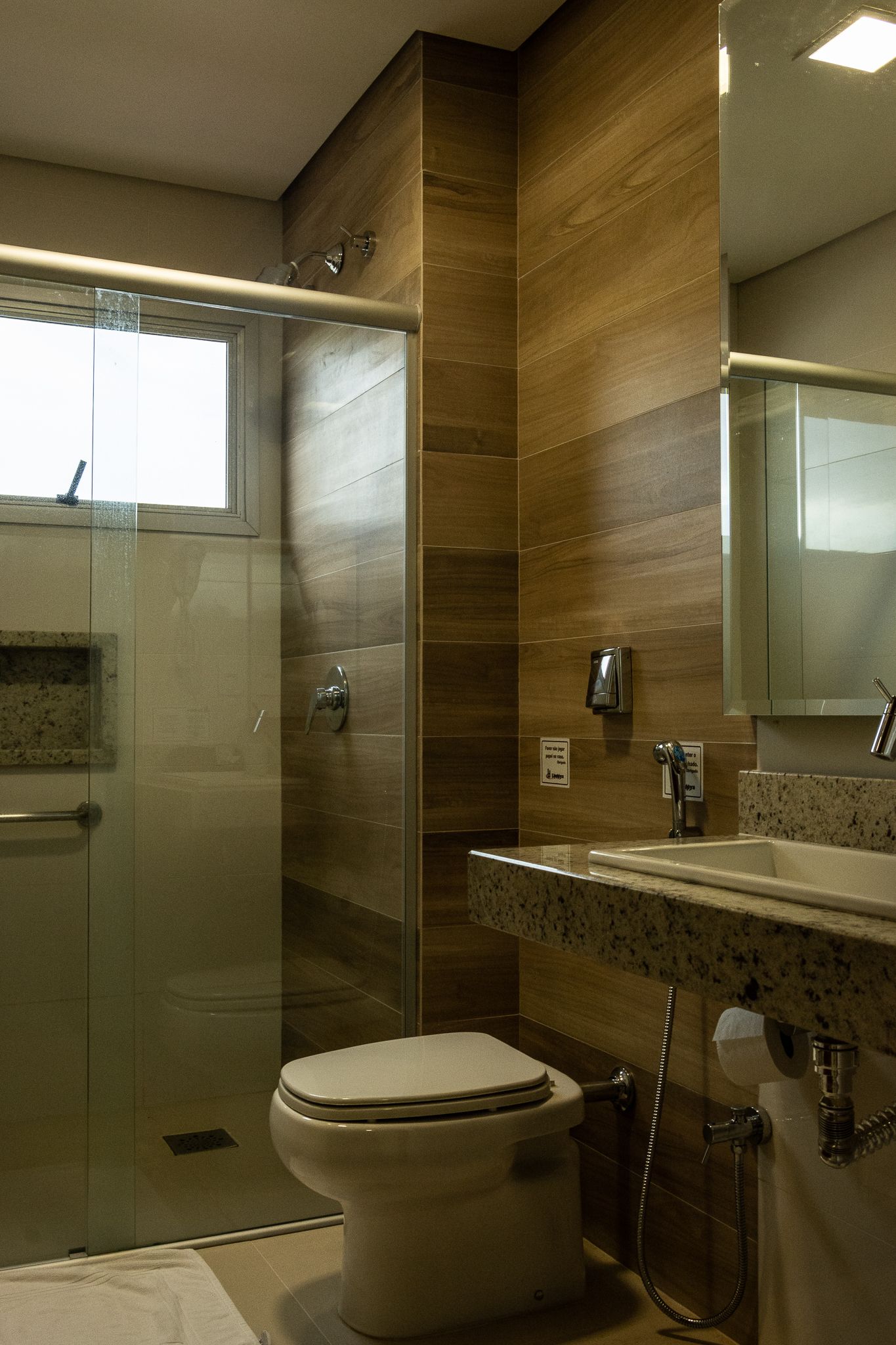 Un baño moderno con cabina de ducha de vidrio, inodoro, lavamanos con encimera de granito y espejo sobre el lavamanos.