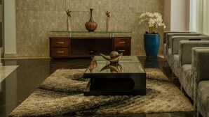 A modern living room with a large, dark-colored sofa, a glass coffee table, and a decorative vase on a wooden cabinet. - Lindoya Hotel (Catalao)