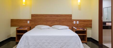 Habitación de hotel con una cama grande, cabecera de madera, dos mesitas de noche y dos lámparas de pared.