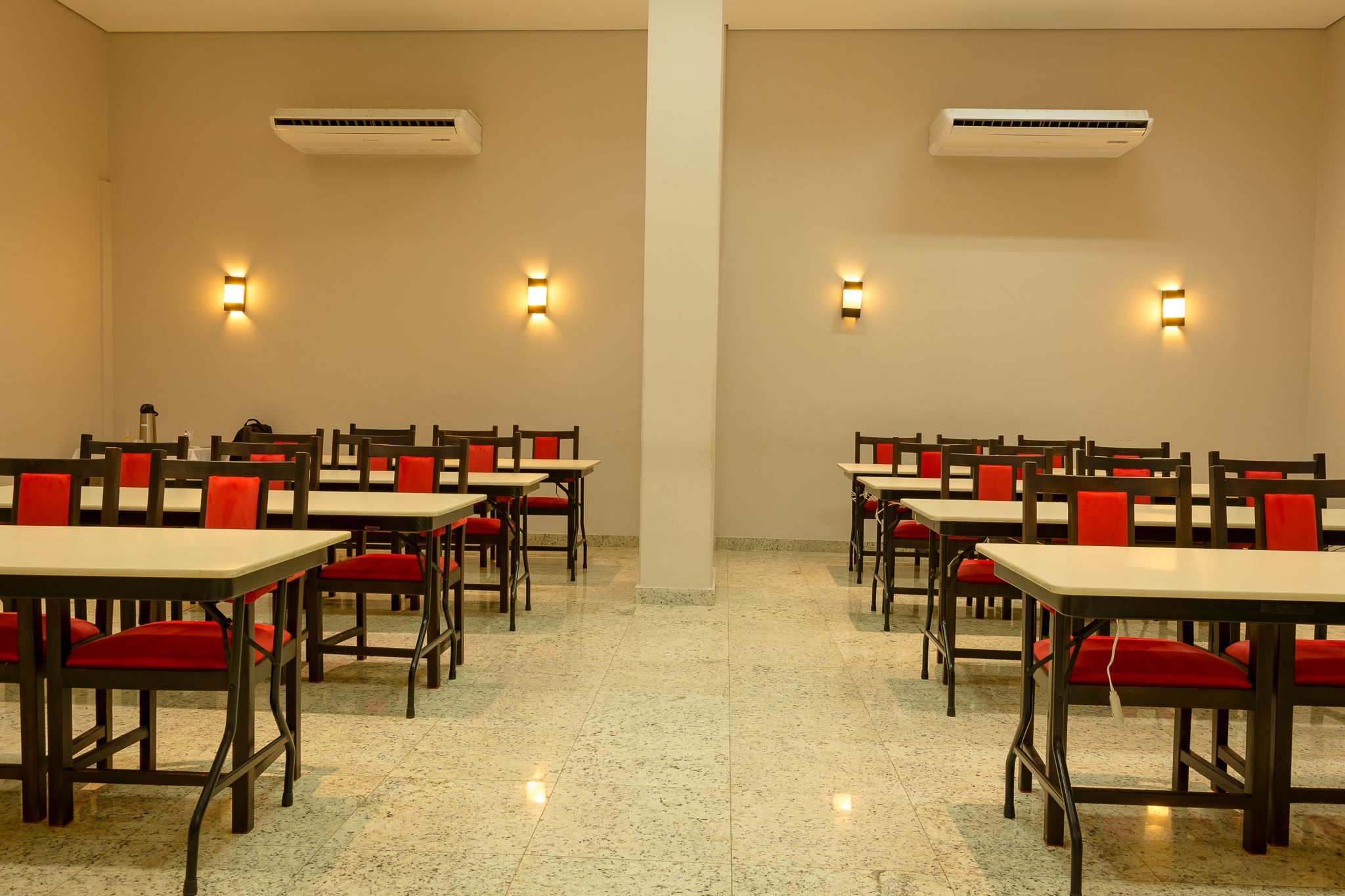Un salón de conferencias con mesas y sillas, unidades de aire acondicionado y luces empotradas en la pared.