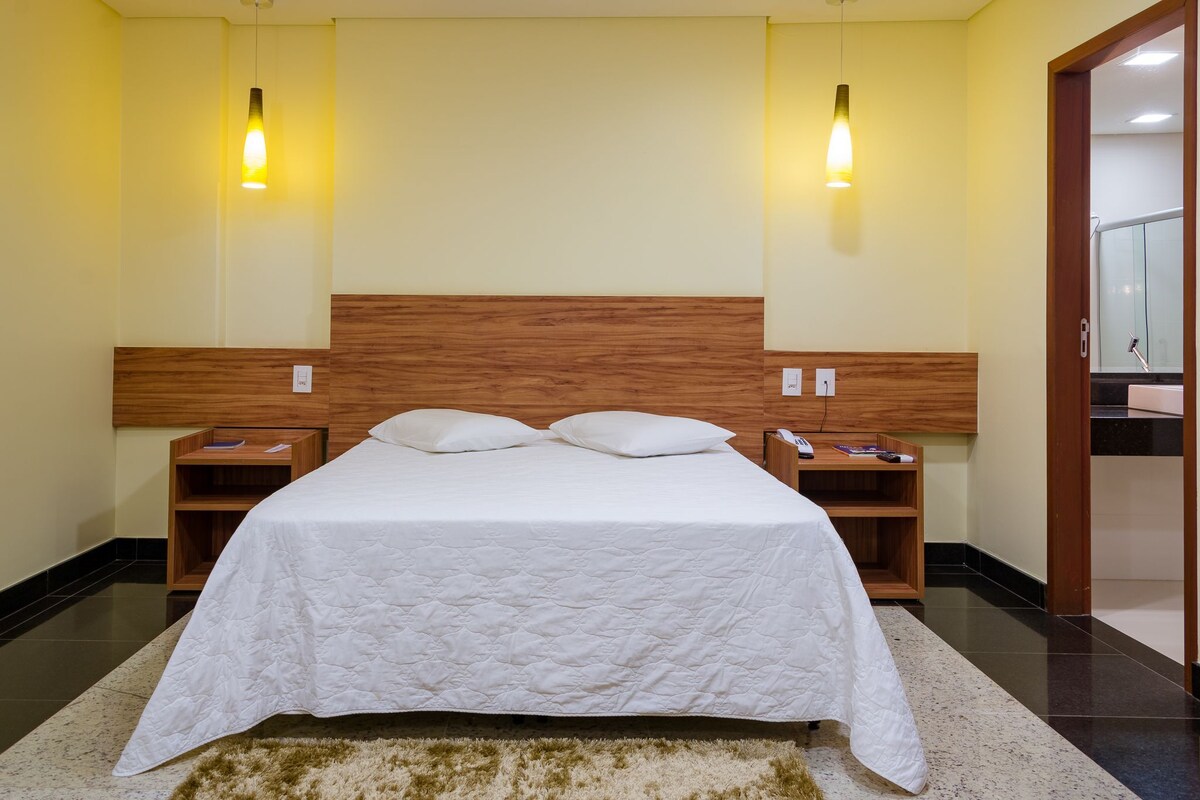 A hotel room with a large bed, wooden headboard, two bedside tables, and a nightstand.