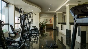 A gym with various exercise equipment, a black-tiled floor, and a potted plant. - Lindoya Hotel (Catalao)