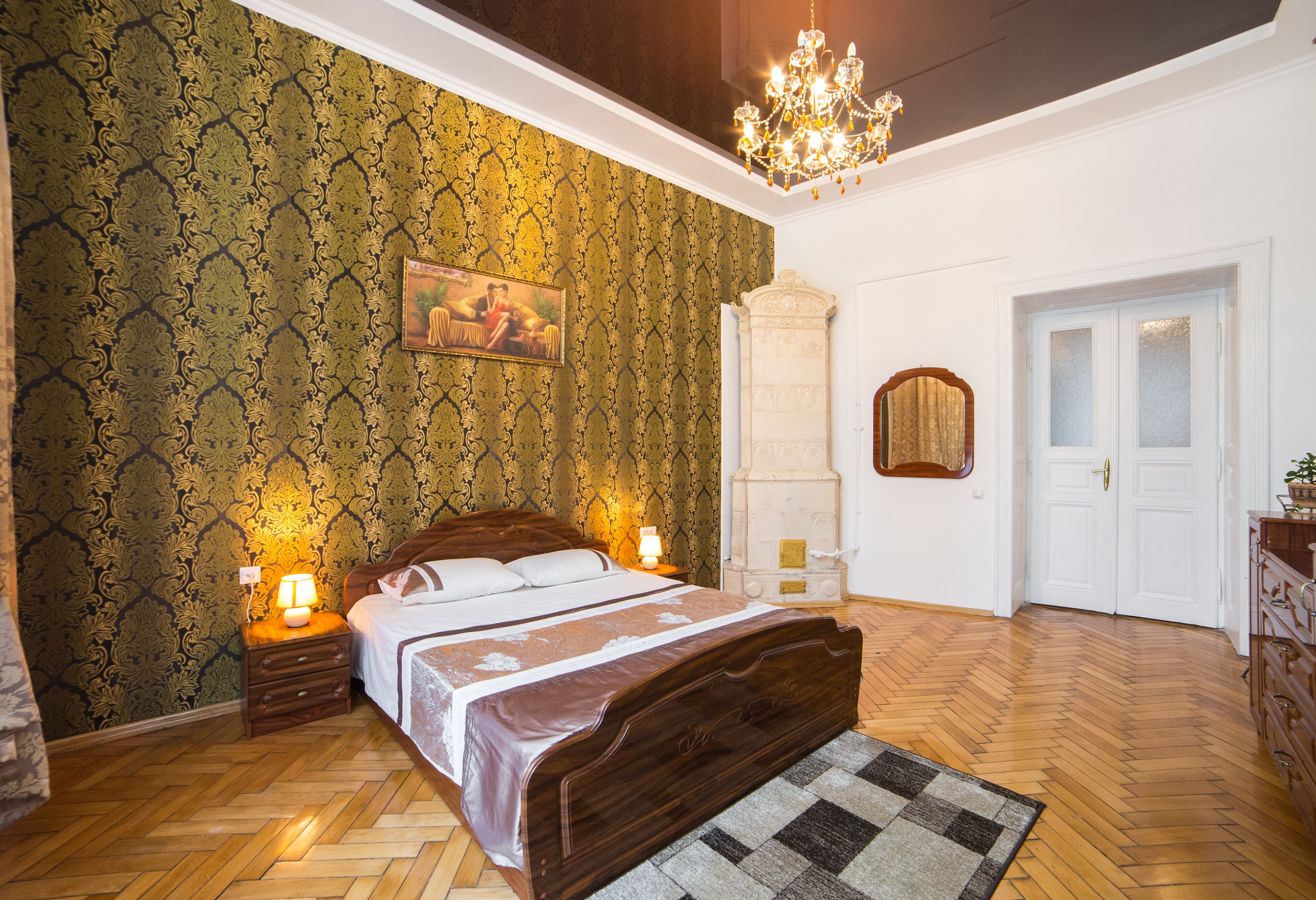 A bedroom with a wooden bed, a chandelier, a patterned wallpaper, and a mirror on the wall.