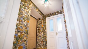 En hall med väggar täckta av mosaik, ett trägolv och en vit dörr med glaspaneler.