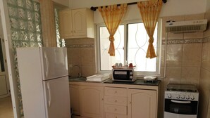 Een kleine keuken met een koelkast, magnetron, fornuis en een raam met gordijnen.