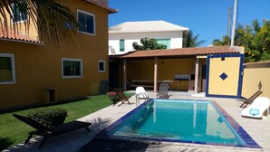 A swimming pool with lounge chairs, a patio area, and a building with a tiled roof. - Casa em Armação de Búzios (Búzios)