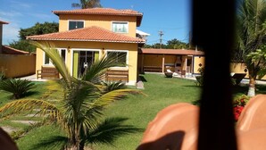 A two-story house with a tiled roof, a front porch, and a well-maintained lawn with palm trees. - Casa em Armação de Búzios (Búzios)
