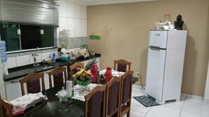 A kitchen with a dining table, chairs, a refrigerator, and a window with blinds. - Casa em Armação de Búzios (Búzios)