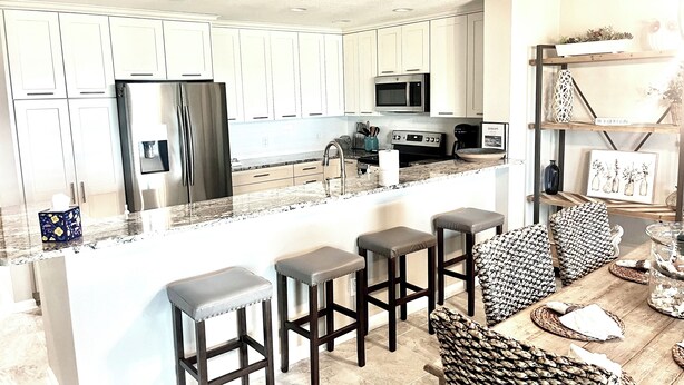 A modern kitchen with white cabinets, stainless steel appliances, and a central island with bar stools. - July 27-Aug 1 open.  Modern Condo—Best location—beach, Ft Clinch & downtown. (Fernandina Beach)