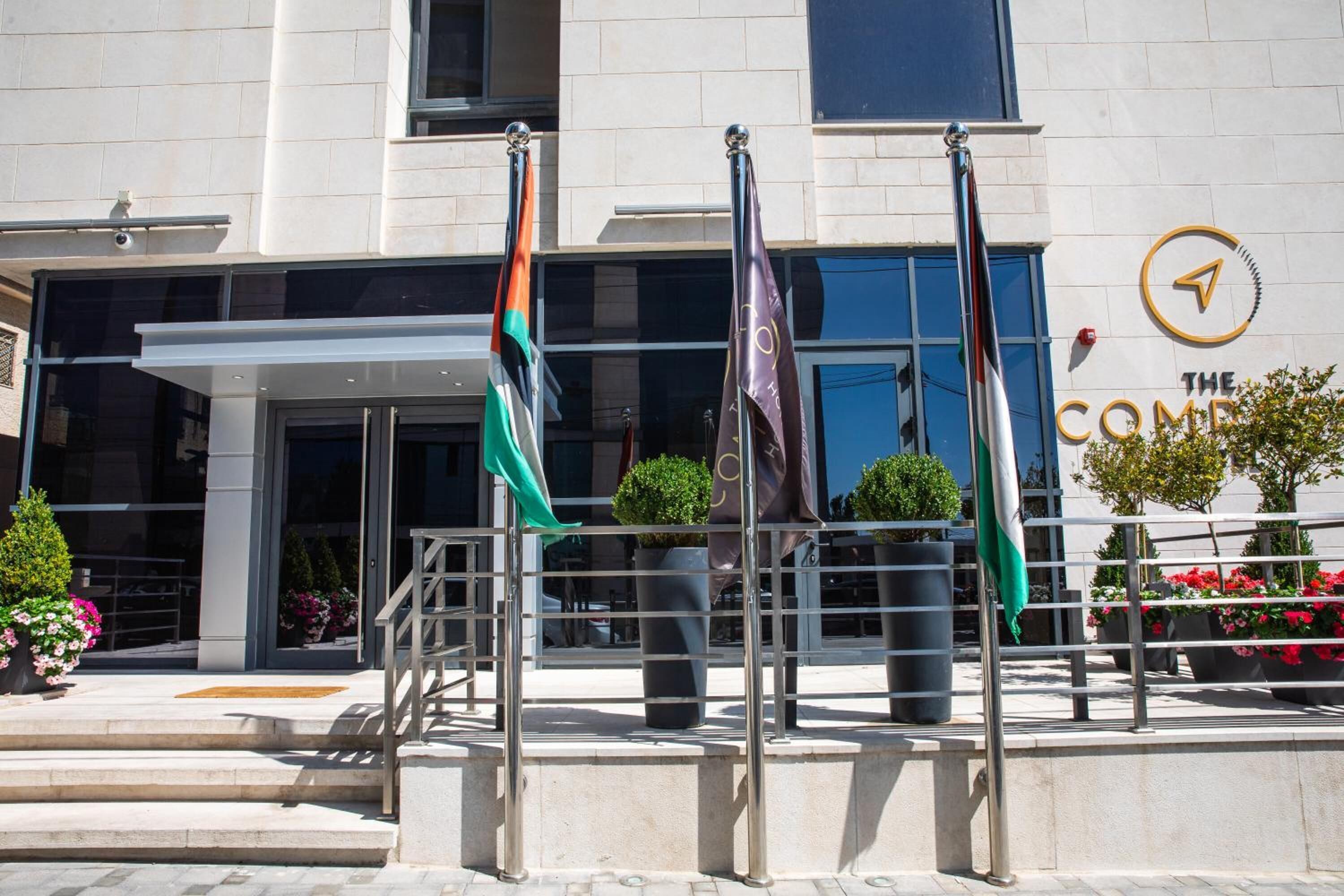 A modern building with a glass entrance, multiple flags, and a sign reading "The Compass."