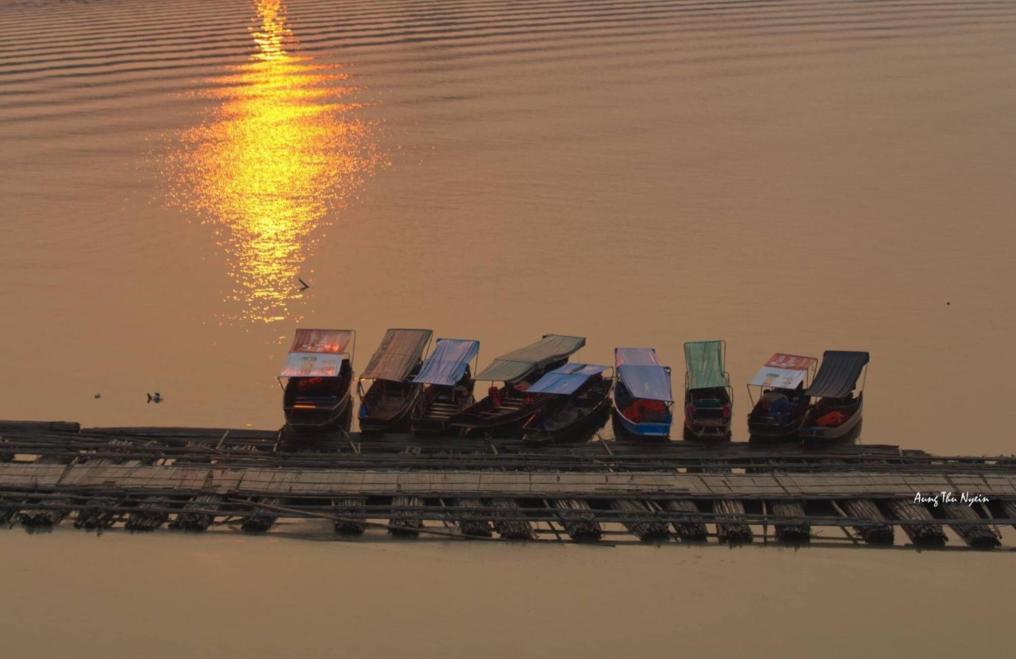 Una fila de barcos estacionados en un muelle, con el reflejo del atardecer en el agua.