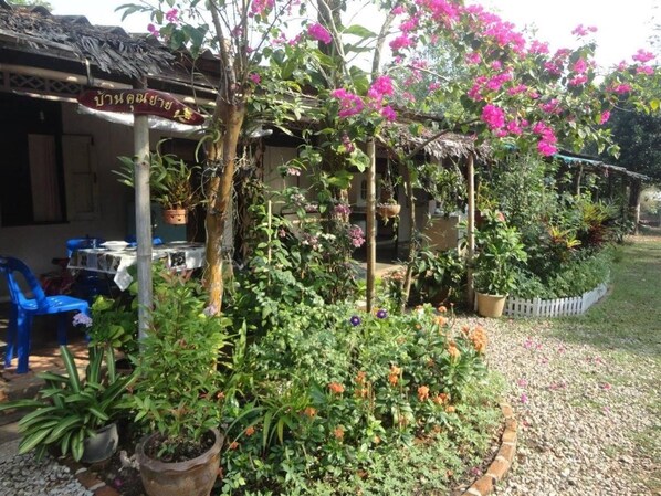 Un jardín con plantas en macetas, una estructura de techo de paja y una cerca de piquetes blancos.