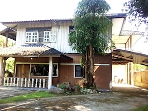A two-story house with a porch, a large tree in front, and a garage. - Grandma's Home Sangkhlaburi (Sangkhla Buri)