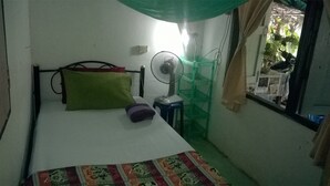A small, simple room with a bed, a standing fan, and a window with curtains. - Grandma's Home Sangkhlaburi (Sangkhla Buri)