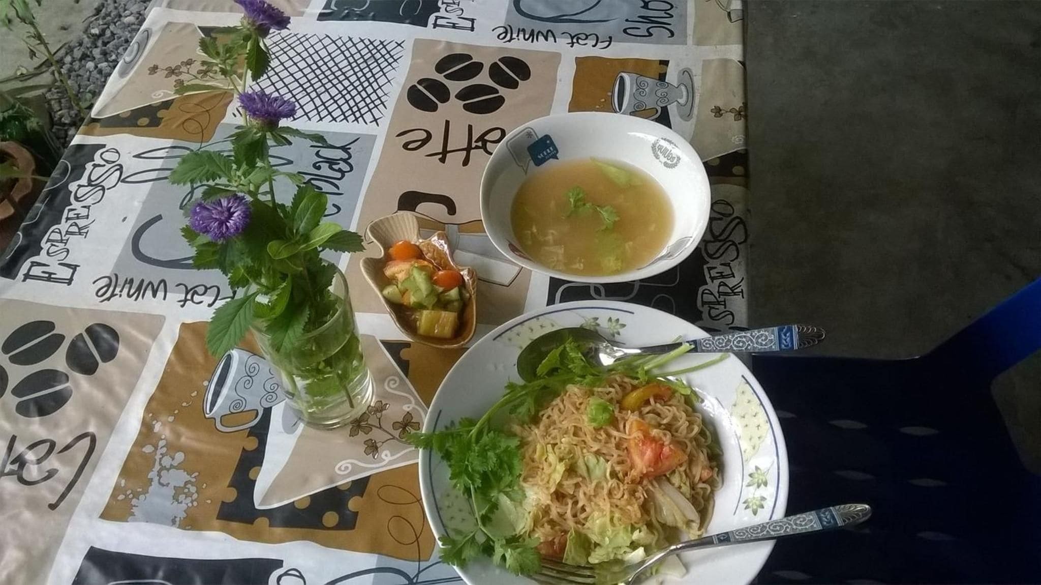 Una mesa con una taza de café, un tazón de sopa y un plato de fideos.
