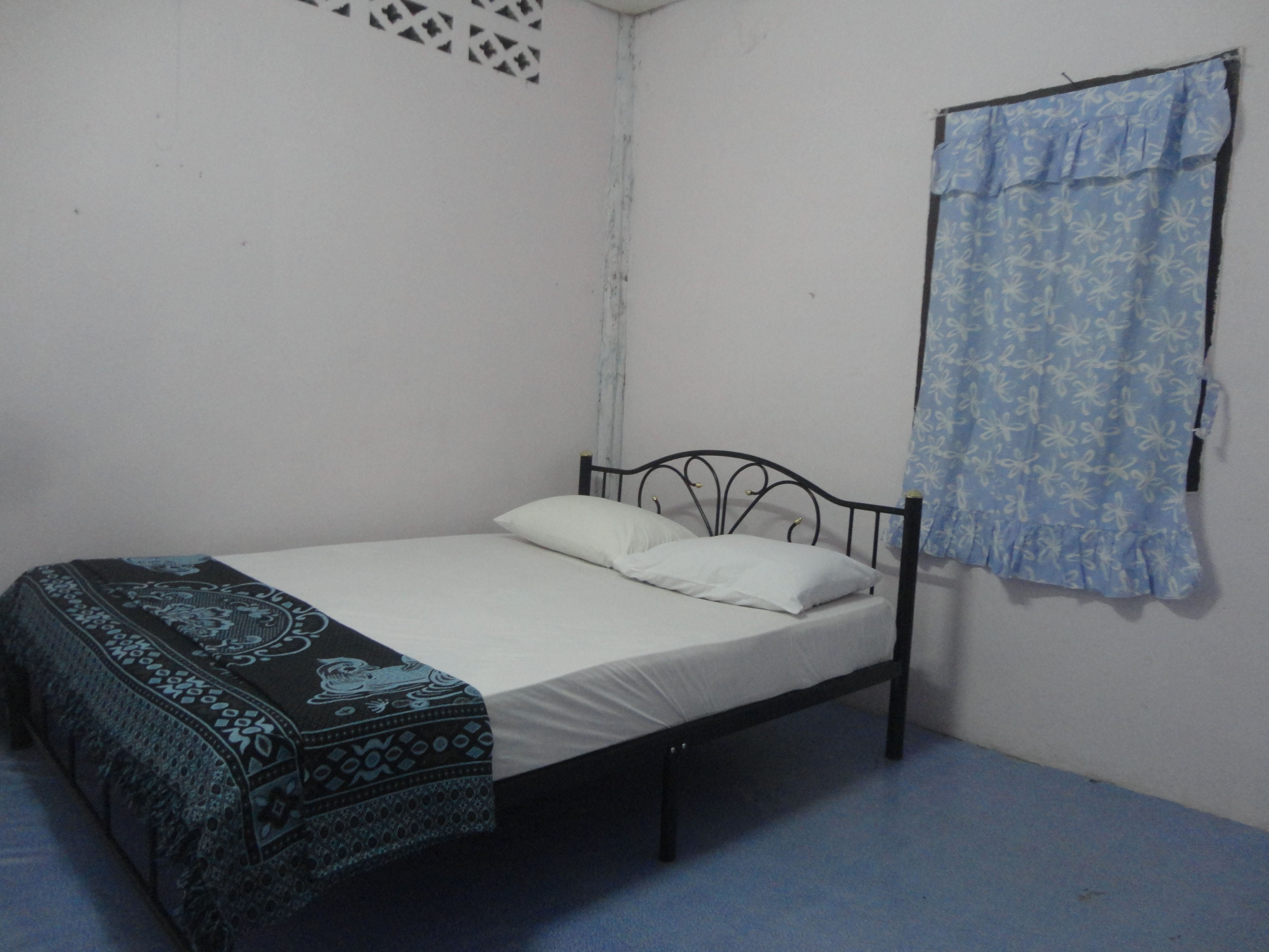 Un lit simple avec un cadre en métal, du linge de lit blanc et une couverture à motifs.
