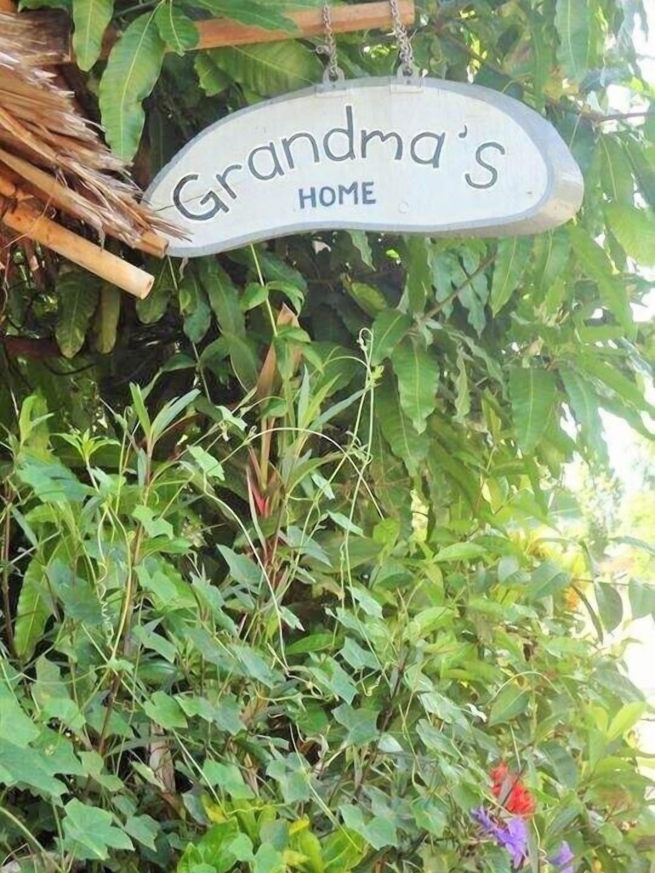 Ein hängendes Schild mit der Aufschrift 'Grandma's HOME' inmitten üppigem Grün.