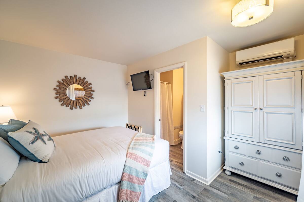 A bedroom with a bed, a TV mounted on the wall, a wardrobe, and an air conditioning unit.