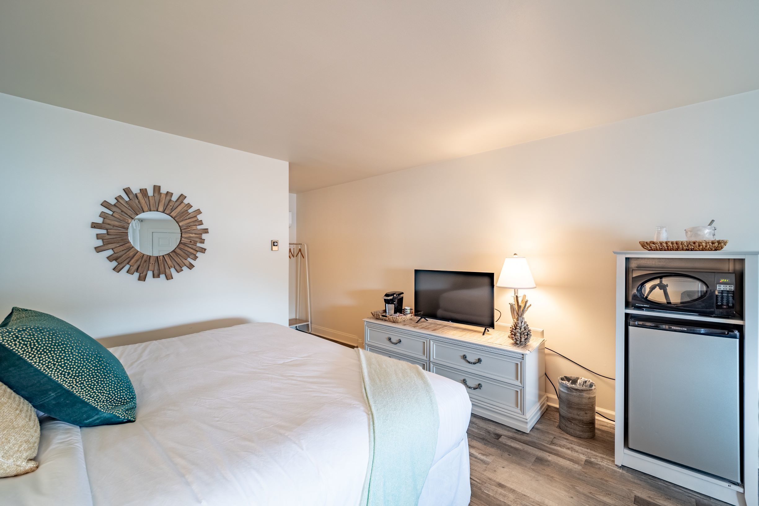 Habitación de hotel con una cama, televisión, microondas y una pequeña mesa con lámpara.