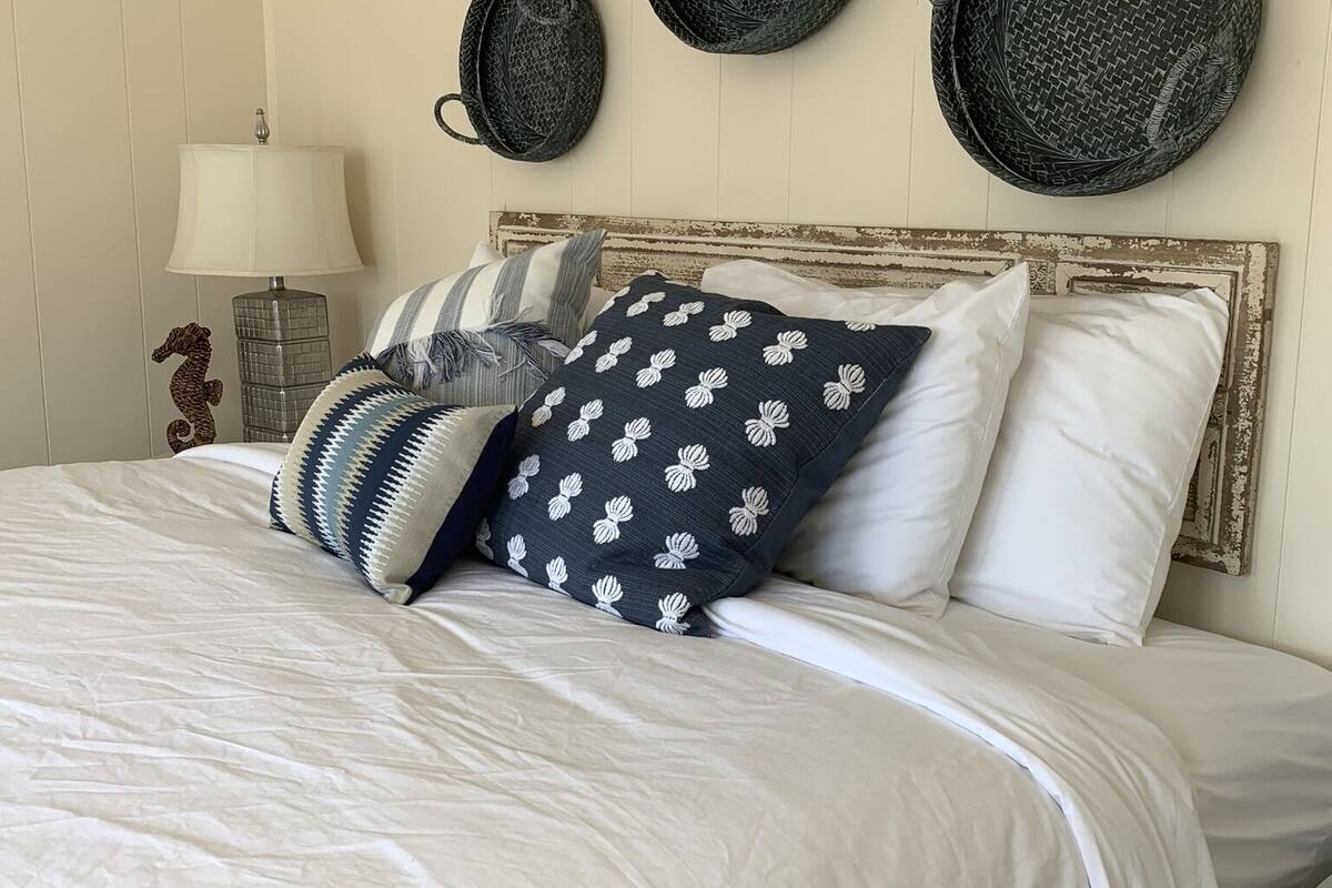 A neatly made bed with a striped throw, a lamp, and three woven plates on the wall.