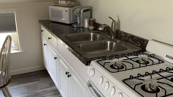 A kitchen with white cabinets, a stainless steel sink, a gas stove, and a microwave.