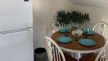A dining area with a white refrigerator, wooden dining table, and white chairs with brown cushions.