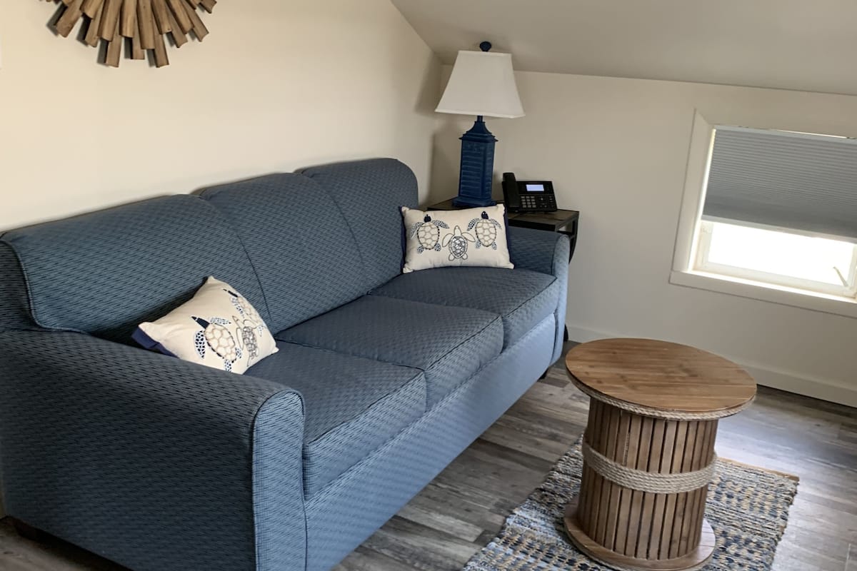 A modern living room with a blue sofa, a round wooden coffee table, a lamp, and a decorative mirror on the wall.