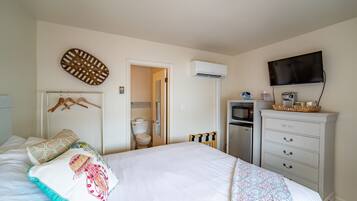 A bedroom with a bed, a dresser, a television, and an air conditioning unit.