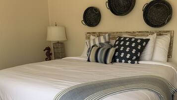 A neatly made bed with a grey throw blanket, a wooden nightstand with a lamp, and three woven baskets on the wall.