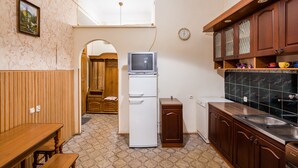 A compact kitchen with a wooden dining table, a white refrigerator, a built-in oven, and dark tiled backsplash. - Apartments on Square Rynok on Theatralna Street (Lviv)