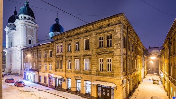 A snow-covered street with historic buildings, including a church with domes and a building with a sign "Gusti Pabek." - Apartments on Square Rynok on Theatralna Street (Lviv)