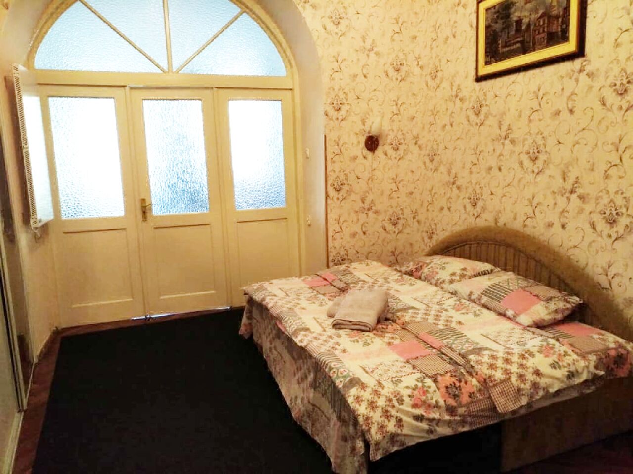 Een slaapkamer met een bed, een deur met geëtste glaspanelen en behang met een patroon.