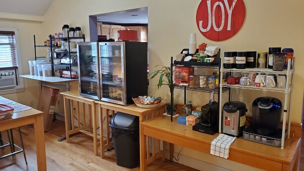 Una kitchenette con refrigerador, cafeteras y un estante con artículos de cocina.