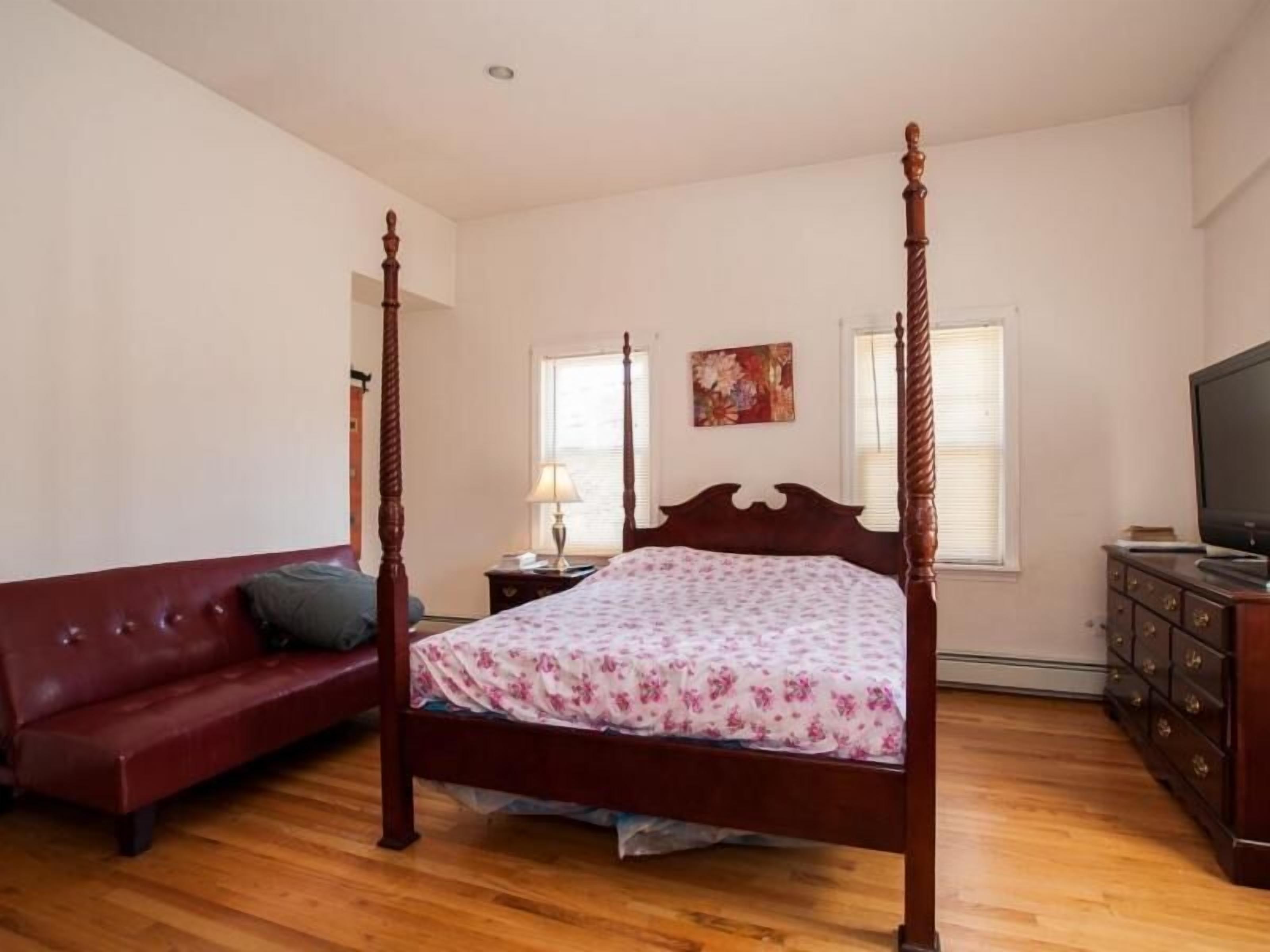 A bedroom with a four-poster bed, a red sofa, a dresser, and a television.