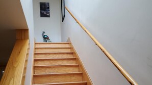 Una escalera de madera con barandilla que lleva a un rellano con un cuadro enmarco y una escultura decorativa de un pájaro.