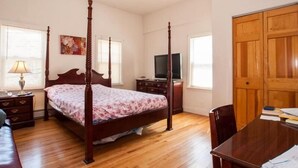 Un dormitorio con una cama con dosel, suelo de madera, un televisor y un armario de madera.